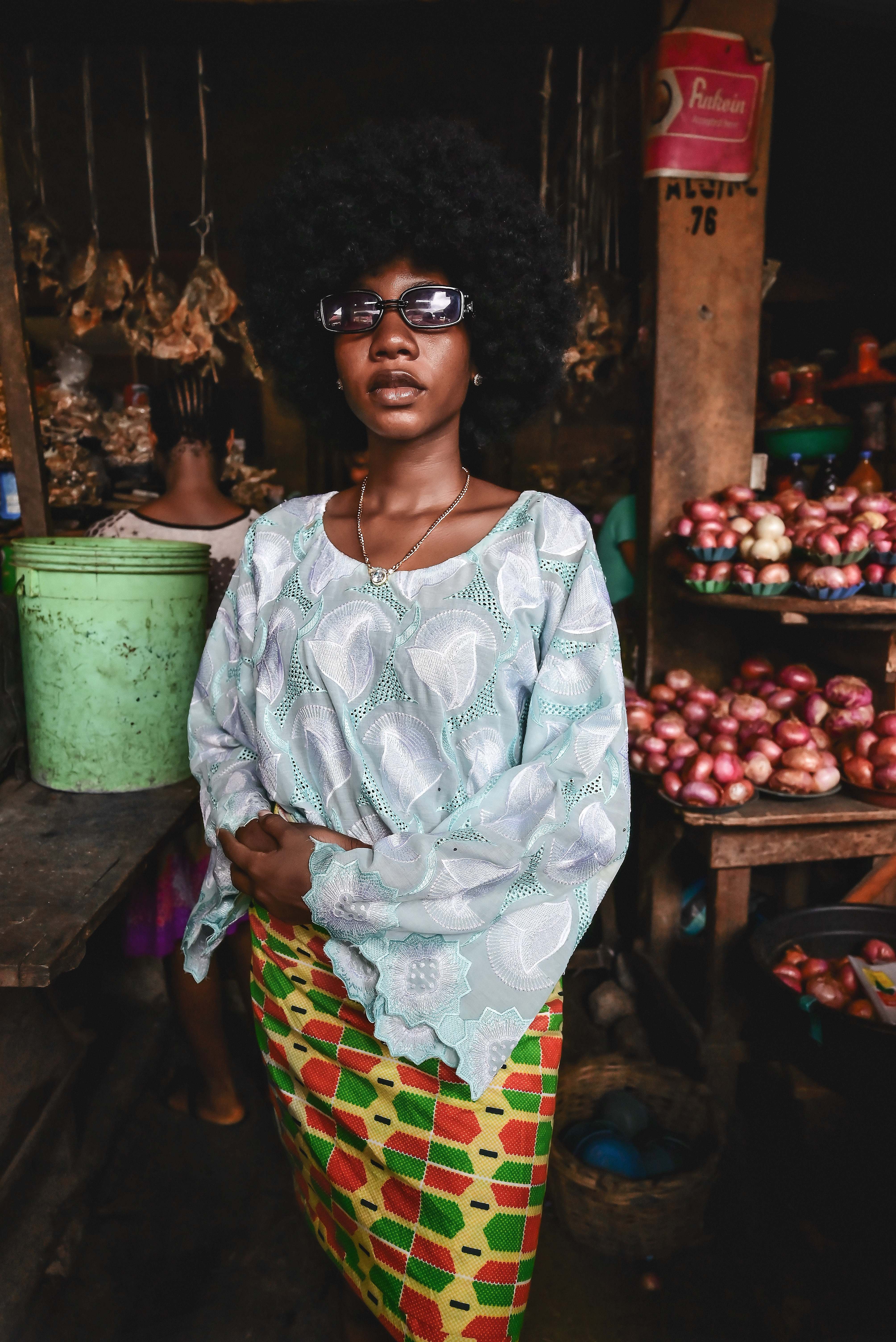 A stylish young Nigerian woman in afro and traditional Ankara fabric standing confidently in a local market
