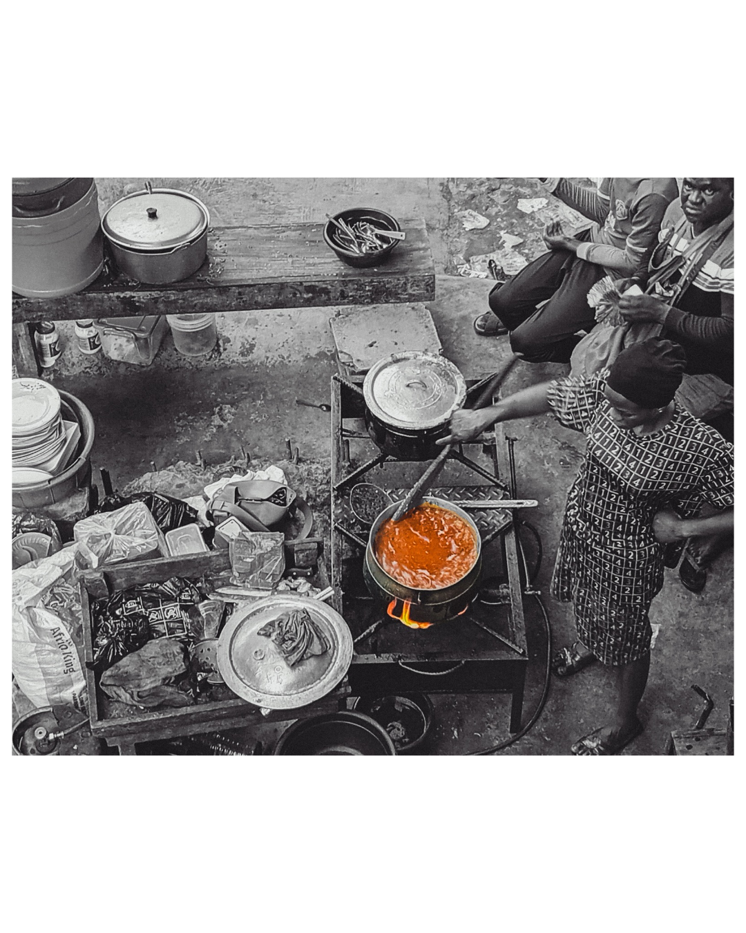 A high-angle selective-color photo of a Nigerian mama put street kitchen, a woman stirring a vibrant orange pot of stew over an open flame